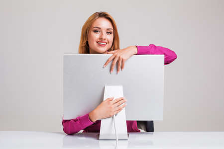young woman sitting in the table and using computer on gray background. satisfied smiling girl hugging Monitorの写真素材