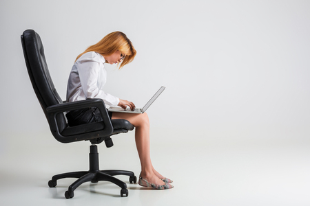 young woman sitting on the chair and using laptop. tired businesswoman under the weight of hard work. hunchbackedの写真素材