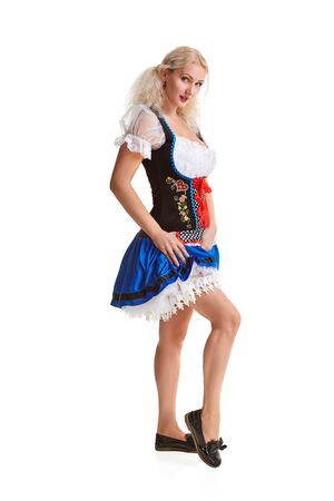 Beautiful young blond girl in dirndl drinks out of oktoberfest beer stein. Isolated on white background. It is a full-length. She lifts her skirt and smilingの写真素材