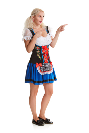 Beautiful young blond girl in dirndl drinks out of oktoberfest beer stein. Isolated on white background. It is a full-length. pointing finger and smiling. copyspace desing conceptの写真素材
