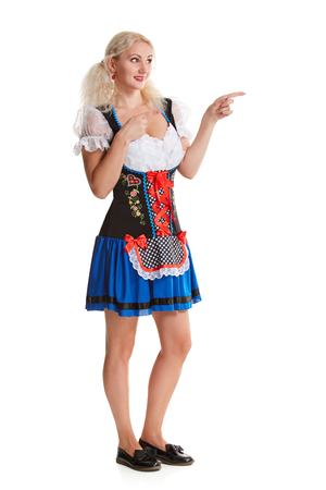 Beautiful young blond girl in dirndl drinks out of oktoberfest beer stein. Isolated on white background. It is a full-length. pointing finger and smiling. copyspace desing conceptの写真素材
