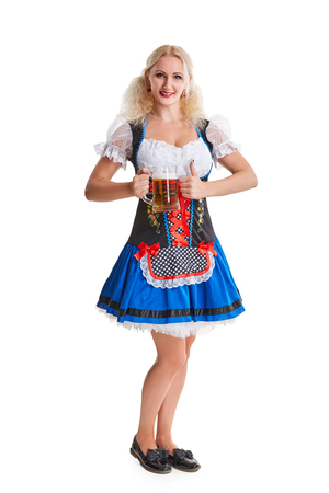 Beautiful young blond girl in dirndl drinks out of oktoberfest beer stein. Isolated on white background. she holds a glass with a drink and smiling. full heightの写真素材