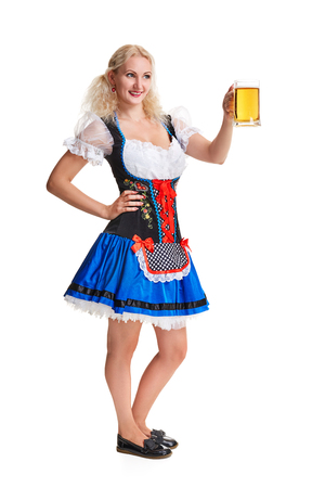 Beautiful young blond girl in dirndl drinks out of oktoberfest beer stein. Isolated on white background. she holds a glass with a drink and smiling. full heightの写真素材