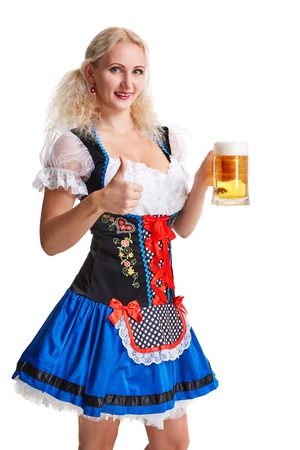Beautiful young blond girl in dirndl drinks out of oktoberfest beer stein. Isolated on white background. she holds a glass with a drink and smilingの写真素材