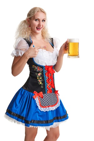 Beautiful young blond girl in dirndl drinks out of oktoberfest beer stein. Isolated on white background. she holds a glass with a drink and smilingの写真素材