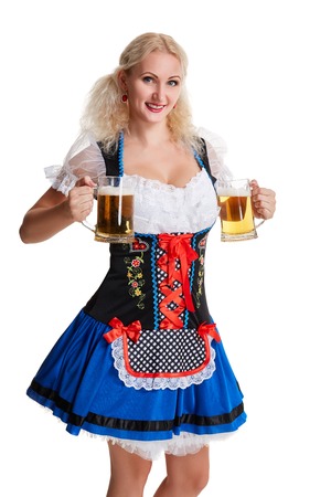 Beautiful young blond girl in dirndl drinks out of oktoberfest beer stein. Isolated on white background. she holds a glass with a drink and smilingの写真素材