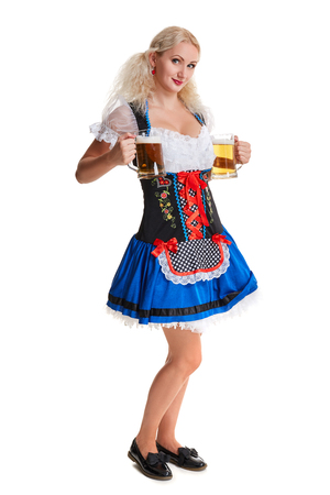 Beautiful young blond girl in dirndl drinks out of oktoberfest beer stein. Isolated on white background. she holds a glass with a drink and smiling. full heightの写真素材