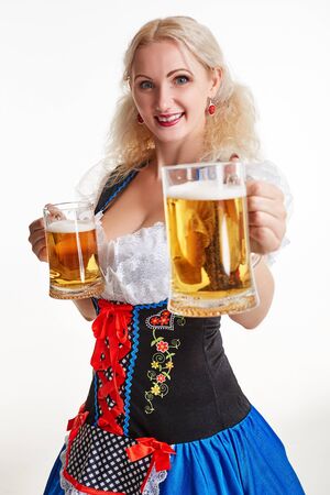 Beautiful young blond girl in dirndl drinks out of oktoberfest beer stein. Isolated on white background. she holds a glass with a drink and smiling. close-upの写真素材