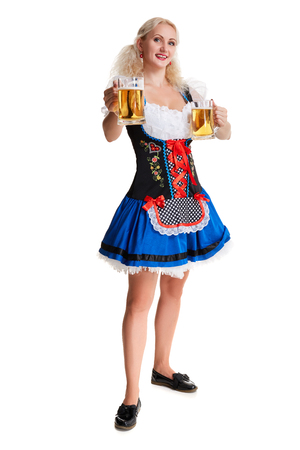 Beautiful young blond girl in dirndl drinks out of oktoberfest beer stein. Isolated on white background. she holds a glass with a drink and smiling. full heightの写真素材