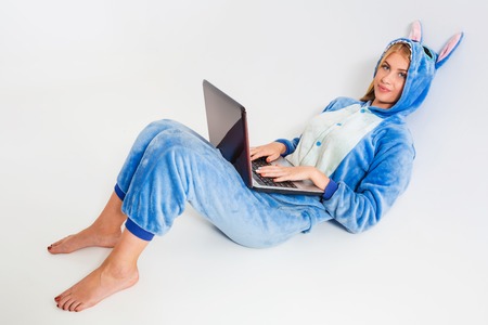 girl in pajamas with a laptop lying on the floor. studying or doing online shopping. work from home. Satisfied and smilingの写真素材