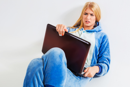 girl in pajamas with a laptop lying on the floor. studying or doing online shopping. work from home. annoyed, surprised, frowningの写真素材