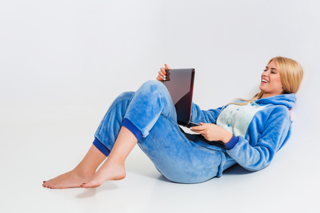 girl in pajamas with a laptop lying on the floor. studying or doing online shopping. work from home. Satisfied and smilingの写真素材