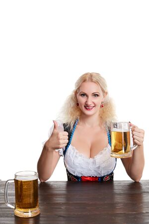 Beautiful young blond girl drinks out of oktoberfest beer stein. Isolated on white background. sits by the tableの写真素材
