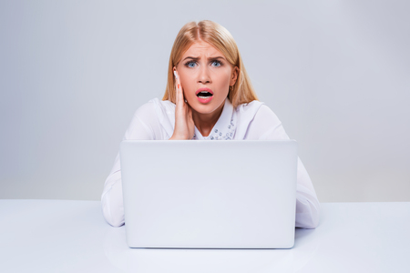 Young businesswoman working at laptop computer. hiding behind the monitor. frustrated, spiteful woman in shockの写真素材