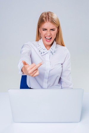 Young businesswoman working at laptop computer. hiding behind the monitor. frustrated, spiteful woman in shock showing middle fingerの写真素材