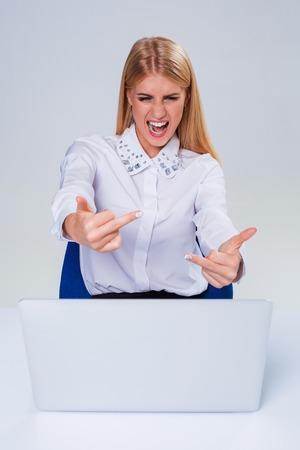 Young businesswoman working at laptop computer. hiding behind the monitor. frustrated, spiteful woman in shock showing middle fingerの写真素材