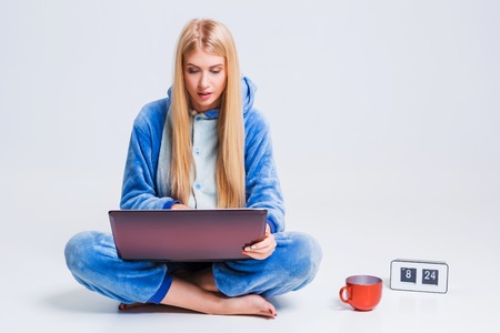 girl in pajamas with a laptop lying on the floor. studying or doing online shopping. work from home. Satisfied and smiling in the morningの写真素材