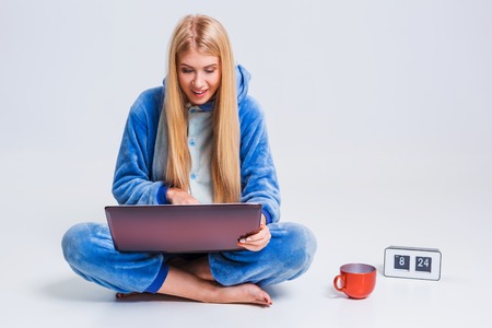 girl in pajamas with a laptop lying on the floor. studying or doing online shopping. work from home. Satisfied and smiling in the morningの写真素材