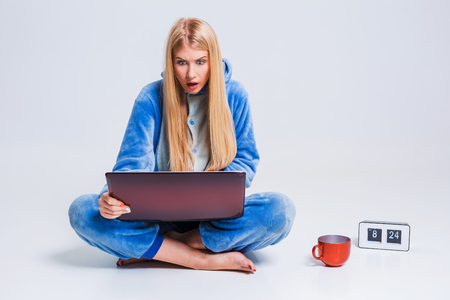 girl in pajamas with a laptop lying on the floor. studying or doing online shopping. work from home. surprise, disgust, asking for helpの写真素材