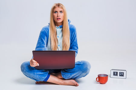 girl in pajamas with a laptop lying on the floor. studying or doing online shopping. work from home. surprise, disgust, asking for helpの写真素材