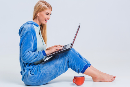 girl in pajamas with a laptop lying on the floor. studying or doing online shopping. work from home. Satisfied and smilingの写真素材