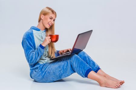 girl in pajamas with a laptop lying on the floor. studying or doing online shopping. work from home. Satisfied and smiling. drinking coffee or teaの写真素材