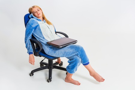 girl in pajamas with a laptop. studying or doing online shopping. work from home. tired of sleeping in a chairの写真素材