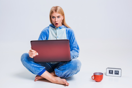 young woman sitting on the floor in his pajamas with a laptop. Working or studying in the morning after sleep. surprised, frustrated, incredulous, looking at the monitorの写真素材