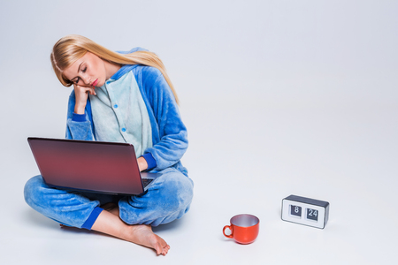 young woman sitting on the floor in his pajamas with a laptop. Morning. Working or studying in the morning after sleep. sleepy looking at the monitorの写真素材