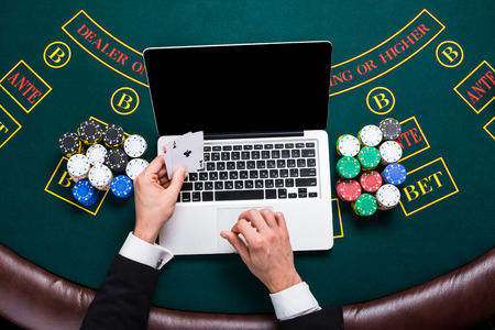 casino, online gambling, technology and people concept - close up of poker player with playing cards, laptop and chips at green casino table. top view. in the hands of two aces, a winning combinationの写真素材