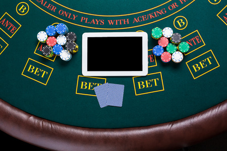 casino, online gambling, technology and people concept - close up of poker player with playing cards, tablet and chips at green casino table. top viewの写真素材