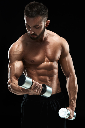 Muscular bodybuilder guy doing posing over black background. dumbbells in his hands. doing exercisesの写真素材