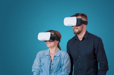 Excited young couple using a VR headset glasses and experiencing virtual reality on grey blue backgroundの写真素材