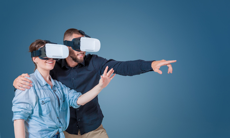 Excited young couple using a VR headset glasses and experiencing virtual reality on grey blue backgroundの写真素材