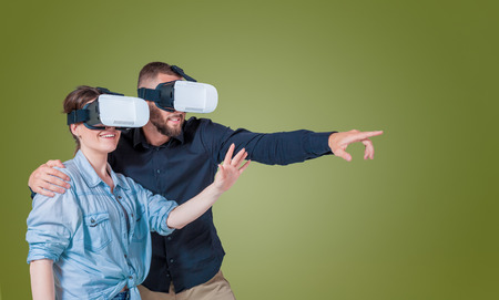 Excited young couple using a VR headset glasses and experiencing virtual reality on grey green backgroundの写真素材