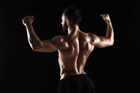 Image of very muscular man posing with naked torso in studio on black background. Rear viewの写真素材