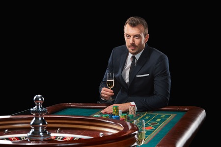 man in a suit playing roulette. addiction to gambling. In the hands of a glass. tensely watching, waiting for the resultの写真素材