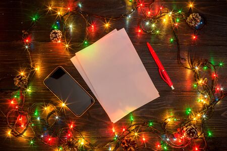 New Year and Christmas mokcup. notebook with Xmas lights on wooden background, space for your text, copyspace. from above. Holiday winter planning concept. Flat lay style.の写真素材