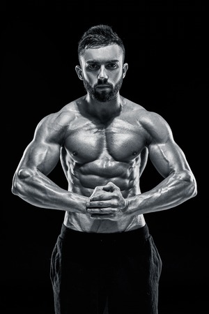 Image of very muscular man posing with naked torso in studio on black background. Black and white colorの写真素材