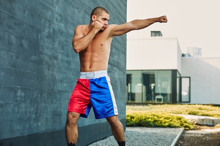 Boxer shorts in athletic training outdoors. He stands in a fighting stance. The young man works off a blowの写真素材