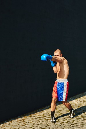 Boxer in multi-colored sports shorts and gloves practicing on the street.の写真素材