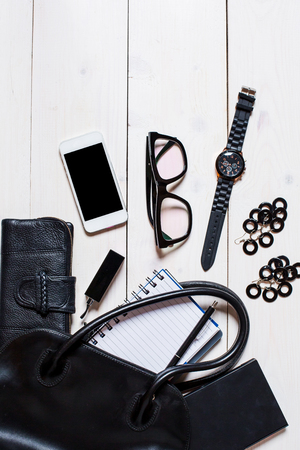 Flat lay, top view, mock up women's accessories fell out of the black handbag on white background. Phone, glasses, watch, notebookの写真素材
