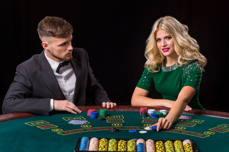 couple playing poker at the table. The blonde girl and a guy in a suit. Woman bets chipsの写真素材