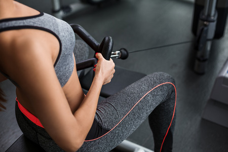 Muscular woman doing exercises on the simulator in the gym. She is wearing a gray tracksuit.