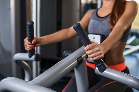 Muscular woman doing exercises on the simulator in the gym. She is wearing a gray tracksuit.の写真素材