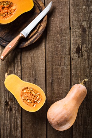 A sliced pumpkin squash on a slate and wooden counter top background. on a board with a knifeの写真素材