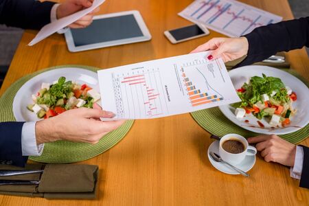 A woman and a man on a business lunch in a restaurant. They pass each other data and graphsの写真素材