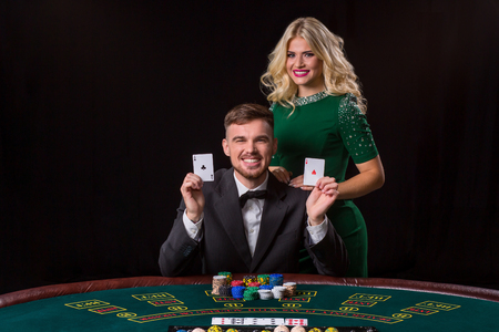 A young man in a suit shows a pair of aces. Playing poker at the table. Young woman enjoys winning at poker. They both look at the camera and smilingの写真素材