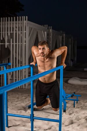 Strong young athlete is engaged in on sports field. Athletic man. Exercises on uneven bars. Athlete Outdoors.の写真素材