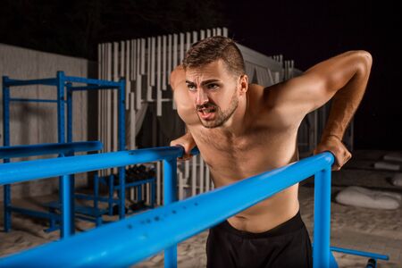 Strong young athlete is engaged in on sports field. Athletic man. Exercises on uneven bars. Athlete Outdoors.の写真素材